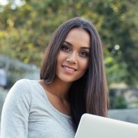 Female student using laptop computer outdoors Portrait of a cheerful female student sitting on the city stairs and using laptop computer outdoors